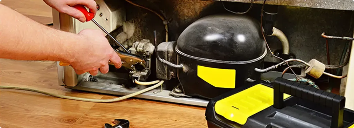 Refrigerator repair technician fixing the compressor and wiring in Elm Grove, WI