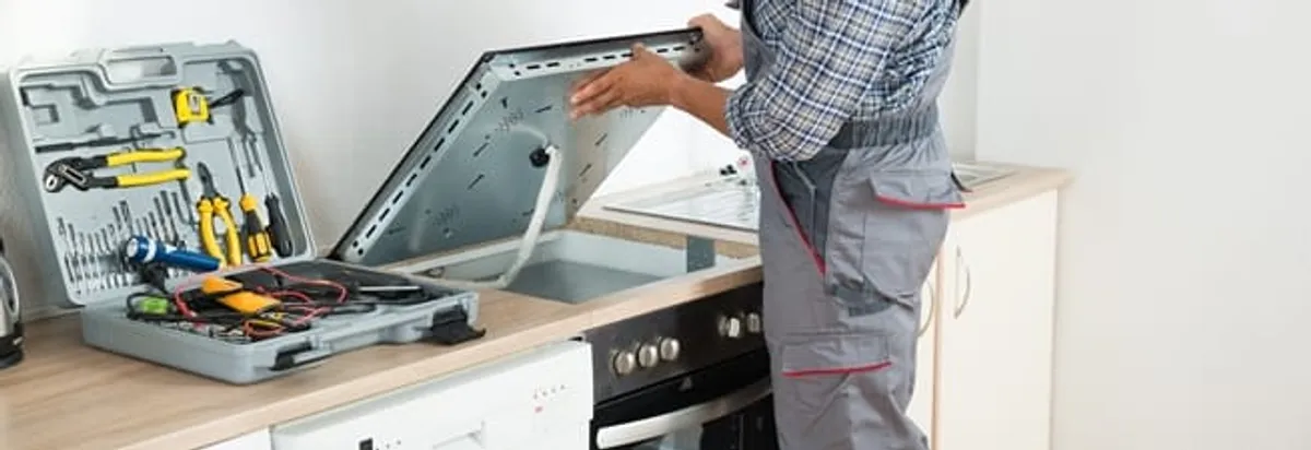 Cooktop repair technician lifting a built-in stovetop for service in Milwaukee, WI